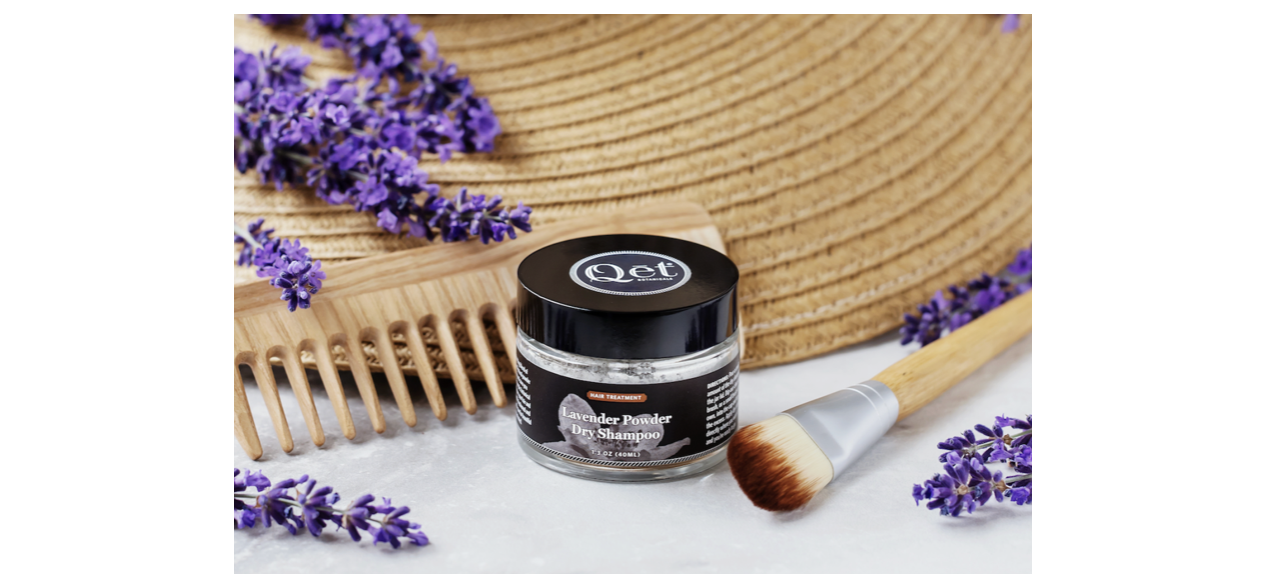 Qet Botanicals Lavender Powder Dry Shampoo with brush, comb, and sprinkled lavender flowers.